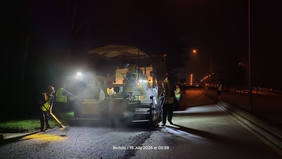 Night paving on the Bintulu Airport road, crew working beside the paver under floodlights