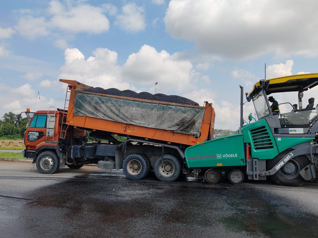Tipper truck feeding premix into a Vögele paver during road resurfacing in Sarawak